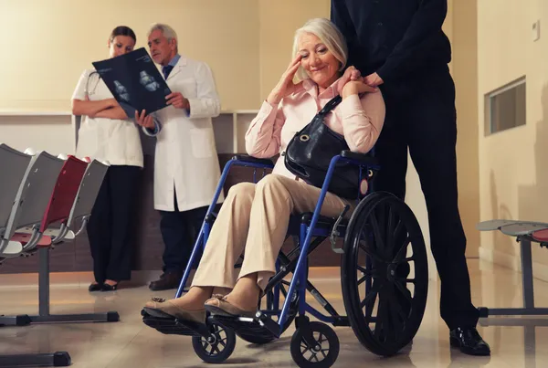 Donna anziana sulla sedia a rotelle con il marito e medici analyzin — Foto Stock