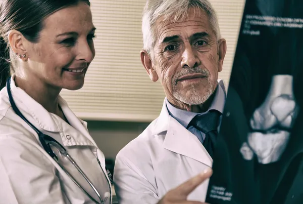 Senior expert male doctor analyzing x-ray scan with his female a — Stock Photo, Image