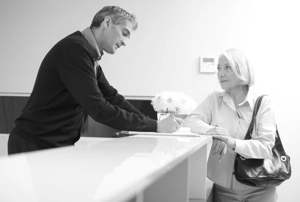 Senior vrouwelijke patiënt bij de receptie ziekenhuis met man in 40s — Stockfoto