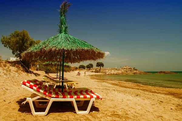 Зелена солом'яна пляжна парасолька з шезлонгами — стокове фото