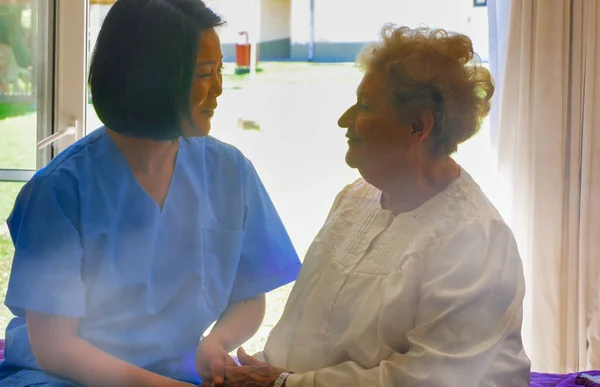 若いですアジアの女性医師と話す高齢者退院女性オンザ病院ベッド — ストック写真