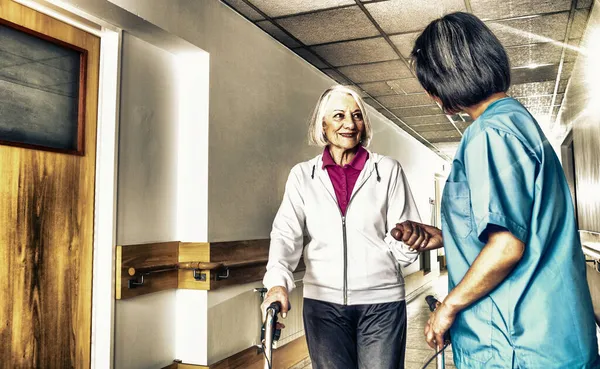 亚洲女医生用步行机安慰成熟的老年妇女 两个女人在医院的过道上开心地笑着 退休社区概念 — 图库照片