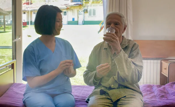年轻的亚洲女医生帮助退休老人在医院病床上吃药 — 图库照片