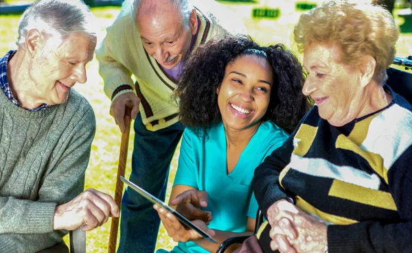 Drie Senioren Ziekenhuis Tuin Leren Gebruiken Tablet Met Verpleegkundige Helpen — Stockfoto
