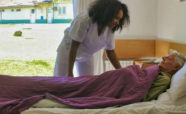 Молодая Африканская Женщина Врач Помогает Пожилым Пенсионерам Лежать Больничной Койке — стоковое фото