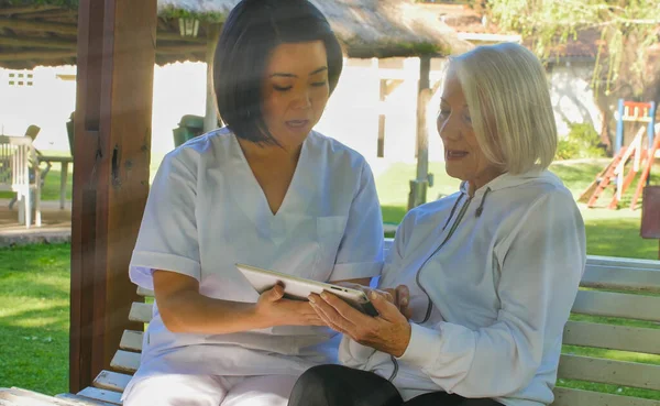 Asyalı Doktor Bahçede Tablet Kullanan Yaşlı Bir Kadına Yardım Ediyor — Stok fotoğraf