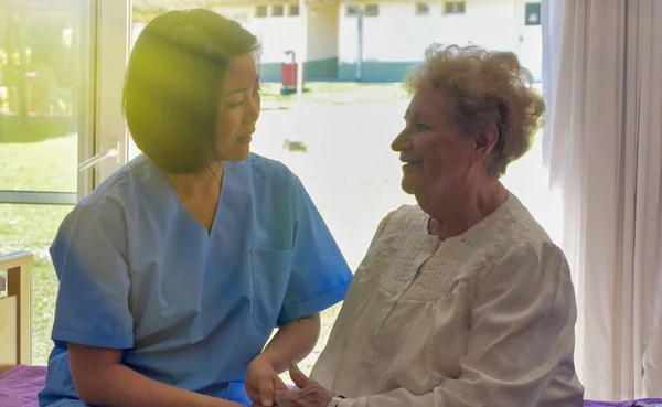 年轻的亚洲女医生在医院病床上与年老的退休妇女交谈 — 图库照片