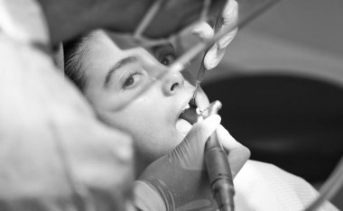 Beyaz lateks eldivenli dişçi dişlerinin durumunu kontrol ederken gülümseyen beyaz kadın. Mavi dişçi koltuğundaki bebek..