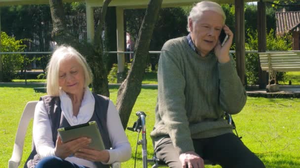 Casal idoso feliz relaxante ao ar livre fazendo chamadas telefônicas. Idosos activos — Vídeo de Stock