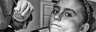 Beyaz lateks eldivenli beyaz dişçi kadın dişlerinin durumunu kontrol ediyor. Mavi dişçi koltuğundaki bebek.