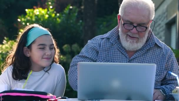 Starszy mężczyzna wyjaśnia wnuczce, jak używać laptopa. — Wideo stockowe