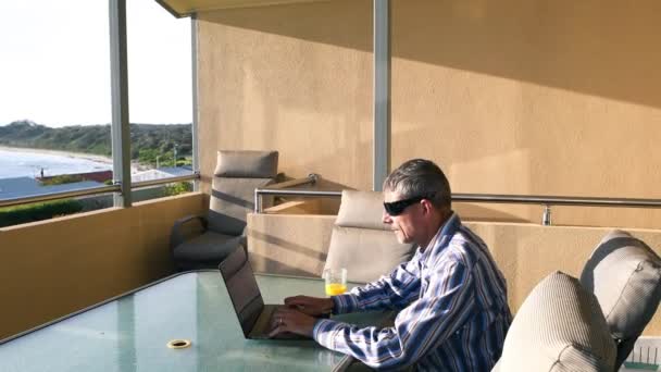 Człowiek pracujący z laptopem na pięknym tarasie z widokiem na ocean. Relaks i koncepcja biznesu — Wideo stockowe