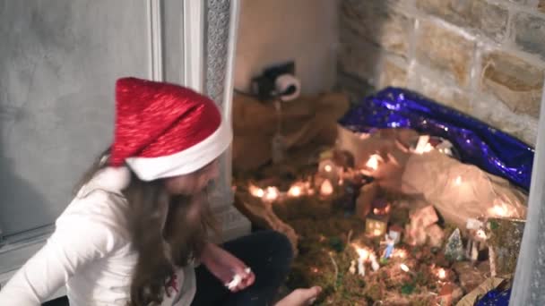 Menina prepara presépio de Natal em casa, usando um chapéu vermelho de Natal — Vídeo de Stock