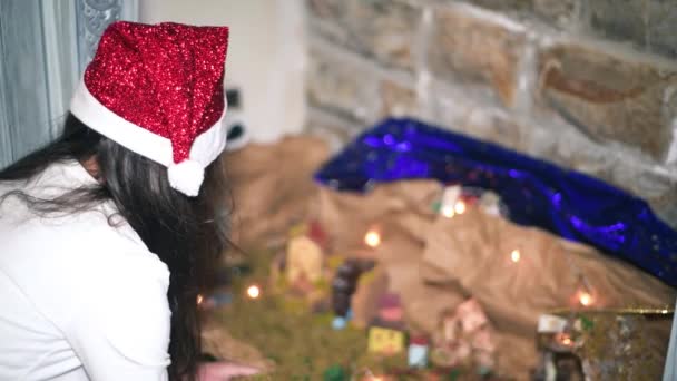 Menina prepara presépio de Natal em casa, usando um chapéu vermelho de Natal — Vídeo de Stock