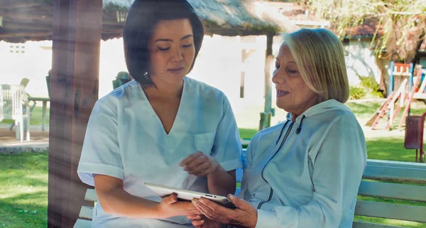 庭のタブレットを使って高齢者の女性を助けるアジアの医師 幸福と退職の概念 — ストック写真