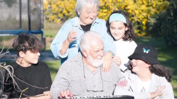 Mężczyzna wyjaśniający, jak używać fortepianu elektrycznego na zewnątrz do swoich wnuków — Wideo stockowe