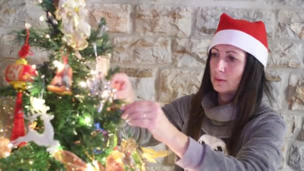 Frau schmückt Weihnachtsbaum zu Hause mit Weihnachtsmütze — Stockvideo