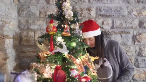 女性は家でクリスマスツリーを飾り、クリスマスの赤い帽子をかぶって — ストック動画