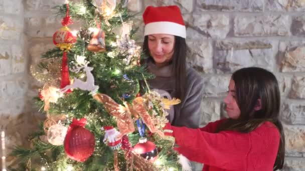 Mulher em casa decorar árvore de Natal com a ajuda de sua filha jovem — Vídeo de Stock