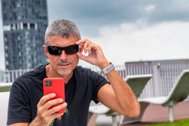 Günlük giysiler içinde bir otel çatısındaki iş mesajlarına bakan bir iş adamı.