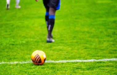 Futbol sahası çizgisi üzerinde futbol topu ve arka planda oyuncu.