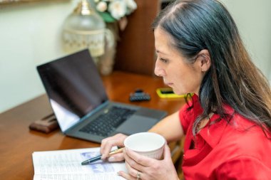 Bilgisayarla çalışan ve stüdyosunda kahve yudumlayan bir kadının yan görüntüsü.