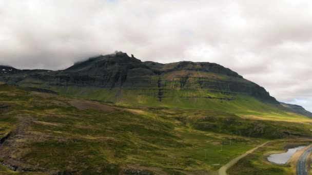 Beroemde IJslandse berg Kirkjufell met meer en oceaan op de achtergrond. Kirkjufell berg op het schiereiland Snaefellsnes in de zomer seizoen vanaf drone uitkijkpunt — Stockvideo