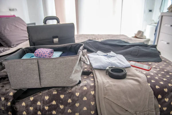 Packing suitcase for business travel. Clothes and briefcase on the bed