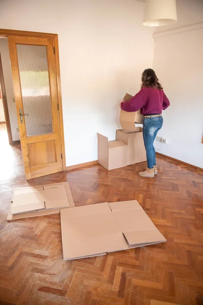 Back view of a woman tidying up cardboard boxes, moving to a new house