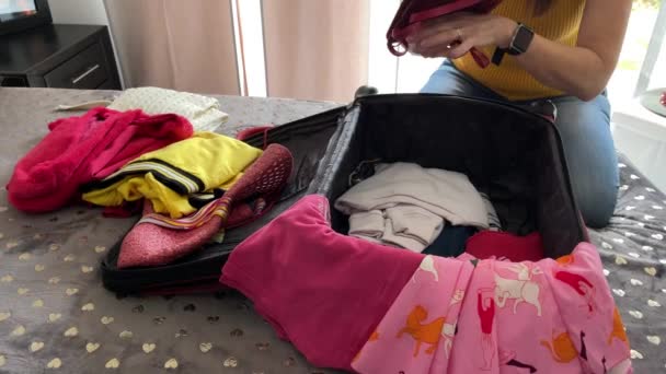 Kvinnliga händer packar sin resväska för en resa. Utsikt över kläder på sängen — Stockvideo