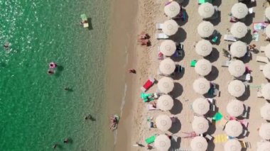 Tropikal bir plajdaki çizgili plaj şemsiyelerinin havadan görünüşü. Yavaş çekim