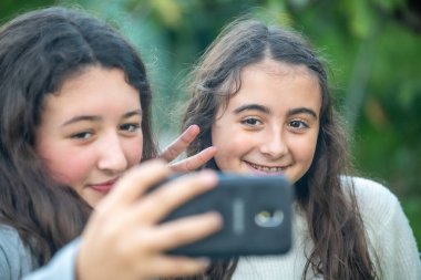 İki genç kız dışarıda akıllı telefonlarıyla selfie çekiyor.