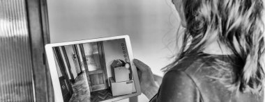 Kadın boş stüdyo dairesini satıp akıllı tabletindeki özel tasarım oturma odasında iç mekanın fotoğrafını çekmeyi planlıyor. Ev satıcı evinde video turu yaptırıyor.