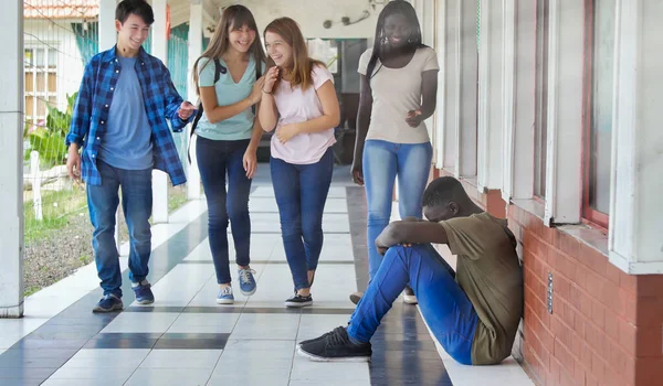 Young boy sitting alone with sad feeling at school. African child in depression abandoned in a corridor and leaning against brick wall. Bullying, discrimination and racism concept.