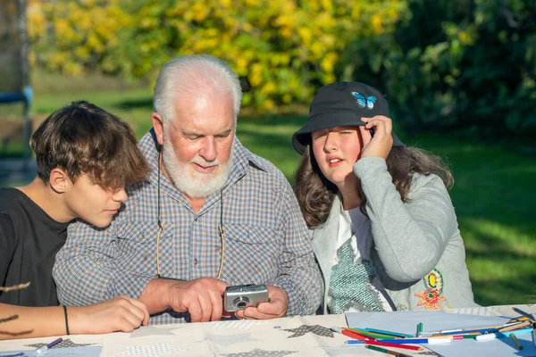 Дедушка Просматривает Снимки Компактной Камеры Открытом Воздухе Своими Внуками — стоковое фото