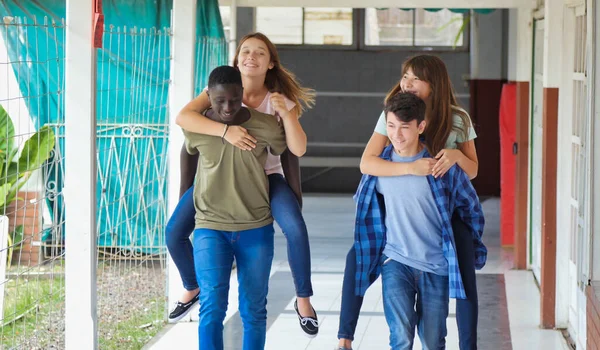 十代のグループの多民族の友人で学校で楽しいPiggyback屋外でザ廊下 — ストック写真