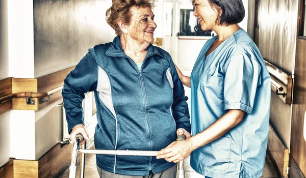 亚洲女医生用步行机安慰成熟的老年妇女 两个女人在医院的过道上开心地笑着 — 图库照片