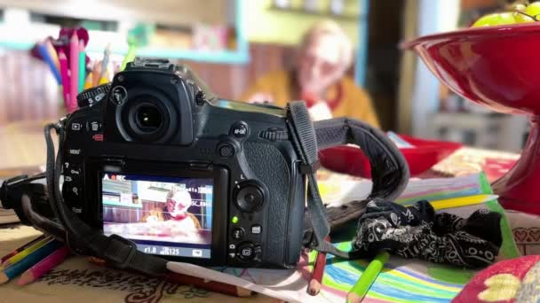 Пожилая женщина пишет на книге дома, современная камера записывает свои действия — стоковое видео