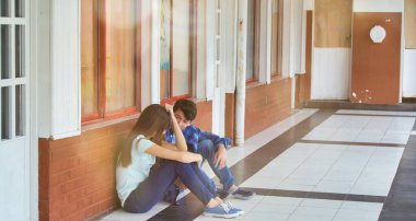 Genç Asyalı kız okulda üzgün bir şekilde yalnız oturuyor. Depresyondaki çocuk bir koridorda terk edildi ve tuğla duvara yaslandı. Zorbalık, ayrımcılık ve ırkçılık kavramı.