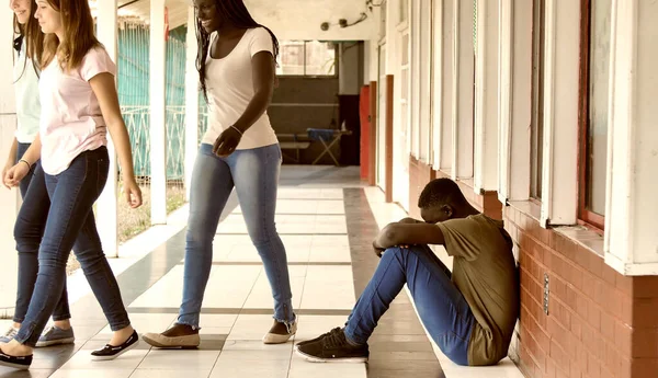 Young boy sitting alone with sad feeling at school. African child in depression abandoned in a corridor and leaning against brick wall. Bullying, discrimination and racism concept.