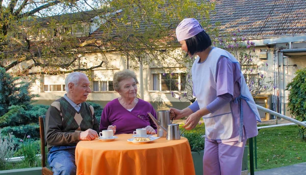 Young asian waitress serving breakfast to elderly retired couple in a hospital rehab garden.