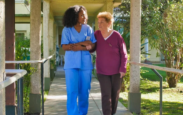 African female doctor talking to elderly retired woman in the hospital yard. Happiness and retirement concept.