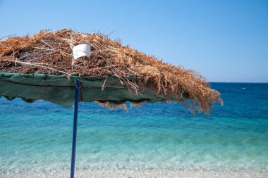 Saman şemsiyesi kıyı şeridi boyunda. Arka planda harika tropikal su var. Tatil kavramı.