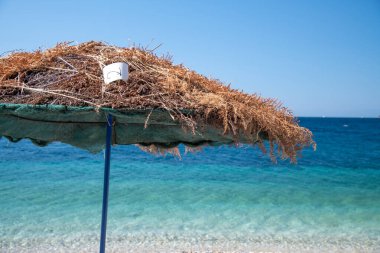 Saman şemsiyesi kıyı şeridi boyunda. Arka planda harika tropikal su var. Tatil kavramı.