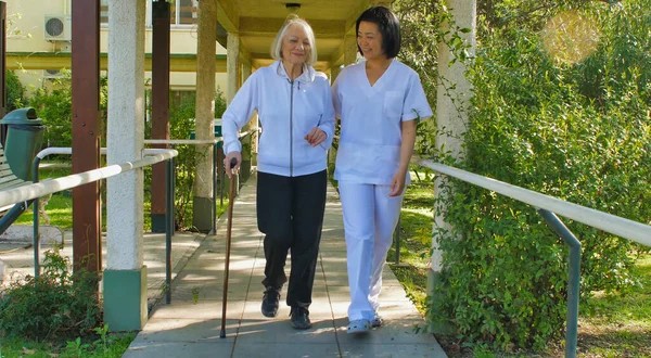 病院の庭にウォーカーの棒で高齢者の女性を助けるアジアの医師 リハビリテーションの概念 — ストック写真