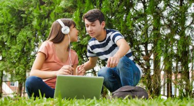 Dizüstü bilgisayar kullanarak çimlerin üzerinde yatan çok ırklı iki genç. Mutluluk ve neşe konsepti.