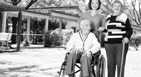 Elder people in rehab facility garden with nurse.