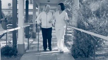 Asian nurse helps elderly woman walking outdoor.