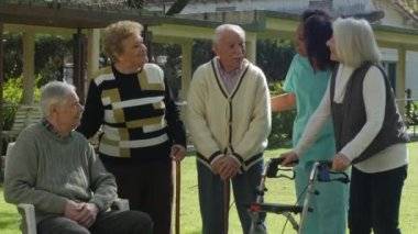 Two couples of elderly active seniors relaxing outdoor with the help of a african nurse.