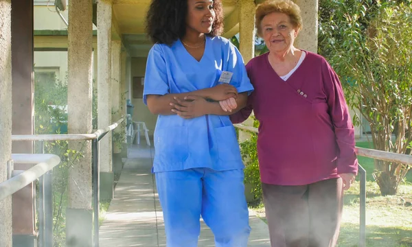 African female doctor talking to elderly retired woman in the hospital yard. Happiness and retirement concept.